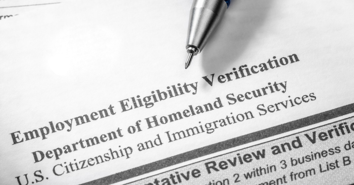 Part of the Form I-9 can be read. A pen tip is visible at top Employment Eligibility Verification Department of Homeland Security U.S. Citizenship and Immigration Services