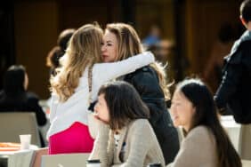 Two women hugging and two women sitting in front of them.