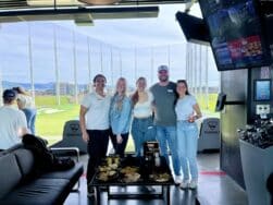 Group standing next to a table with food. Golf course in the background.